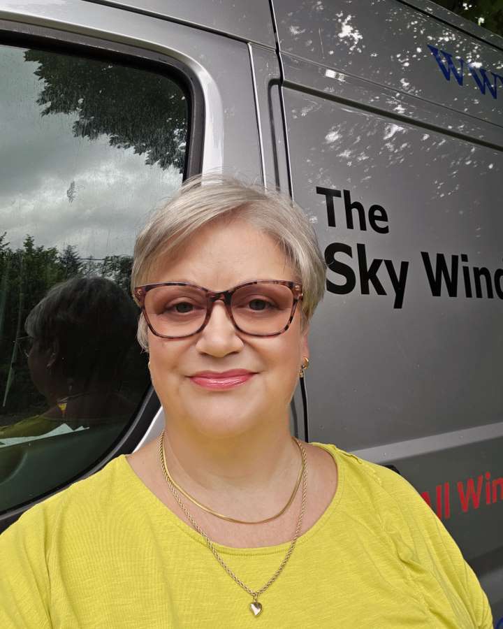 Team member photo of a woman with large brown glasses, blonde hair and a yellow tshirt on